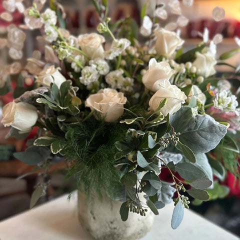 Bouquet of white and beige flowers in a clear vase on a table with a blurred background.