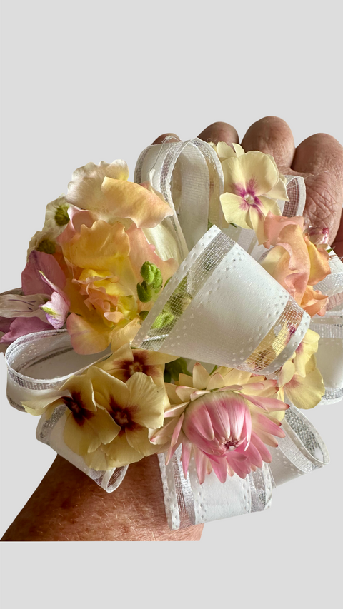 Hand holding a floral corsage with ribbons against a light background