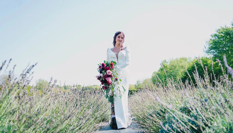 Woman in a white dress holding a bouquet of flowers in a lavender field.